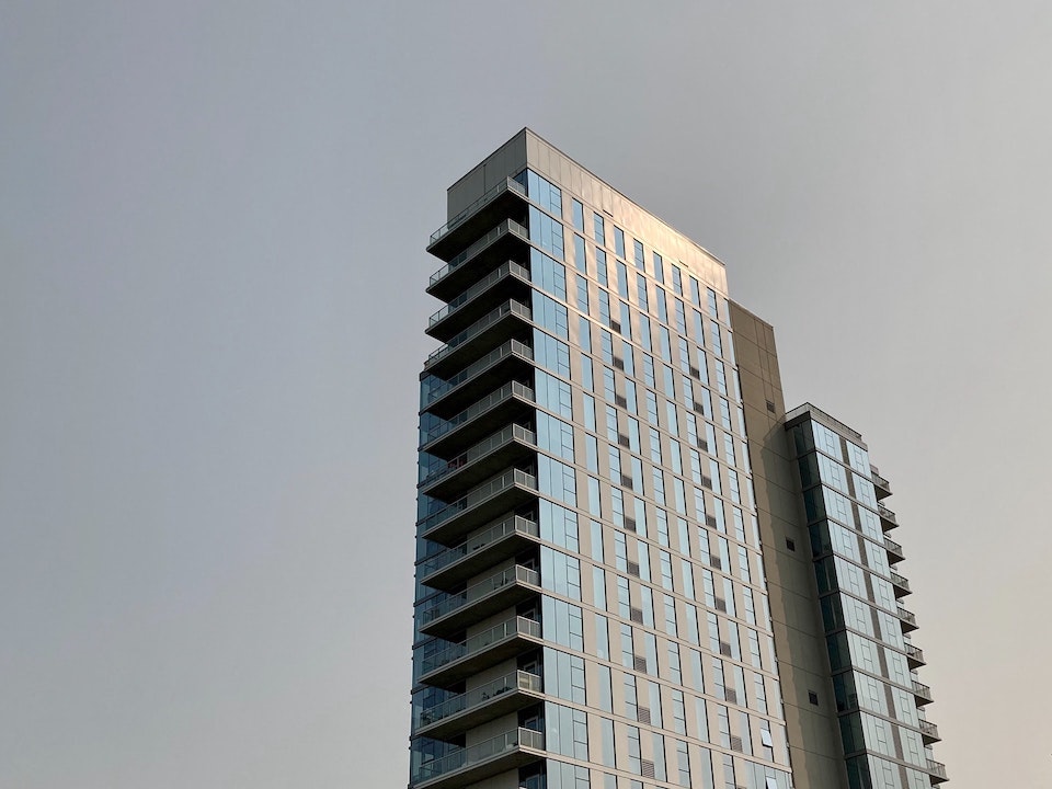 A tall building, made of glass and steel, reflects the yellow morning sunshine, against a cool grey-blue sky.