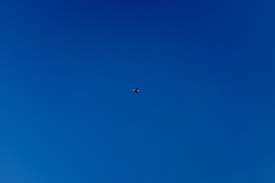 A plane, in bright sunlight, cuts across a blue sky.