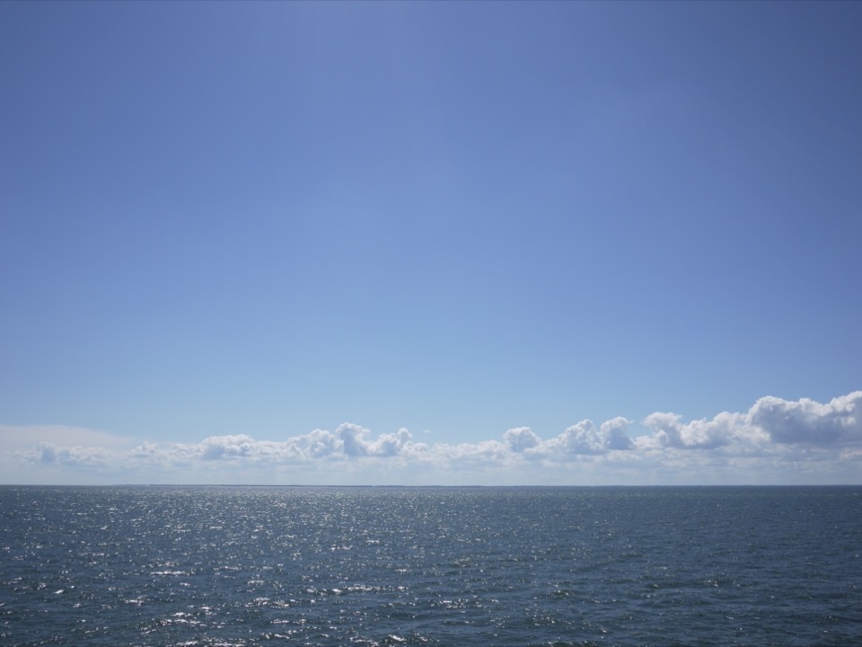 White clouds over the ocean, floating in a bright blue sky.