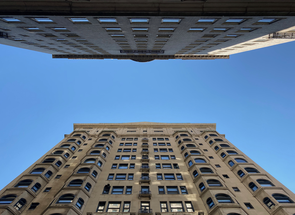 Two large apartment buildings, on the opposite sides of a Philadelphia street toward the alley of blue sky between them.